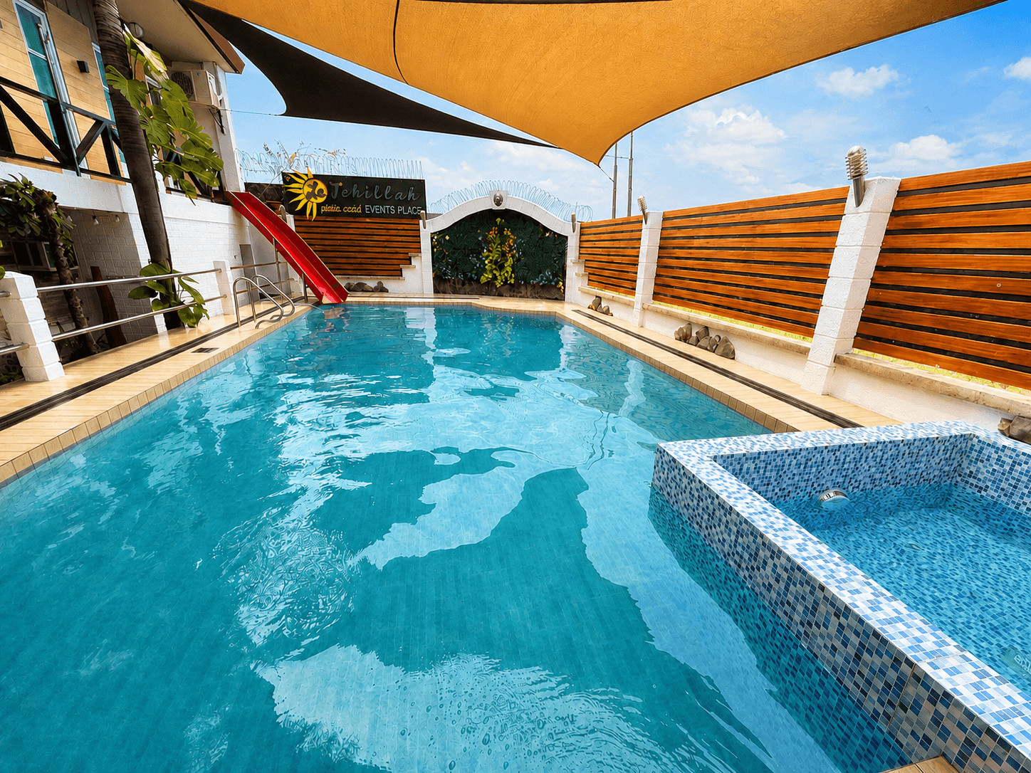 Main swimming pool with red water slide and shade sails at La Tehillah Private Resort